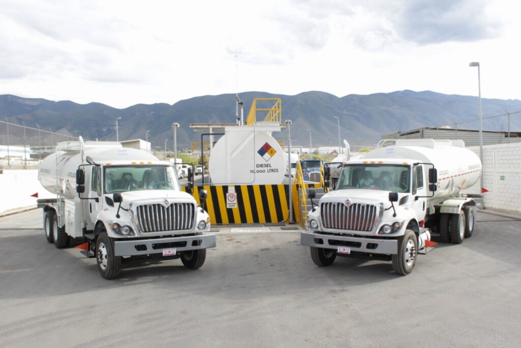 2 Tráilers blancos estacionados junto a un tanque inustrial estacionado.